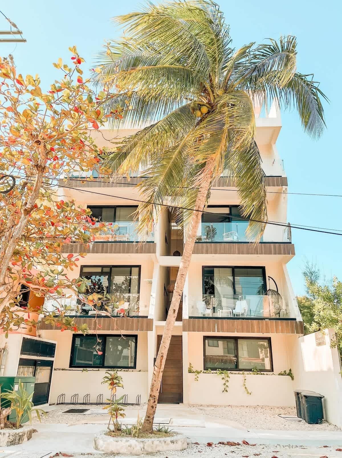 A multi-story building with balconies, a palm tree, and a garden area.