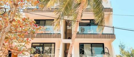 A multi-story building with balconies, a palm tree, and a garden area.