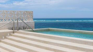 A pool with steps leading to the water, a clear sky, and the ocean in the background.