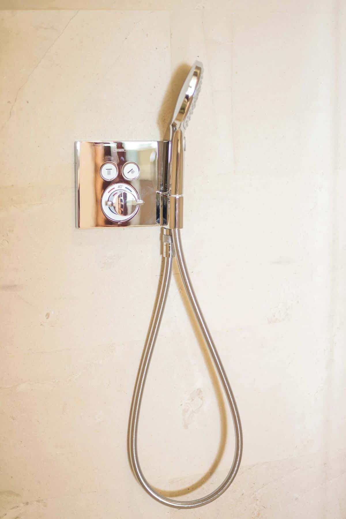 A chrome shower fixture with a flexible hose and a wall-mounted control panel with temperature and water flow settings.