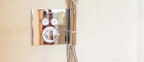 A chrome shower fixture with a flexible hose and a wall-mounted control panel with temperature and water flow settings.