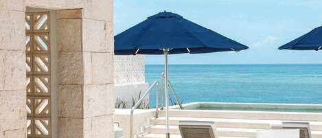 Un espace de détente extérieur avec vue sur la mer, comprenant des chaises longues, des parasols et une pergola agrémentée de guirlandes lumineuses.