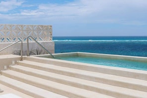 A pool with steps leading to the water, a clear view of the ocean, and a patterned fence in the background. - PH Tucán: Private Terrace and Ocean View rooftop (Puerto Morelos)