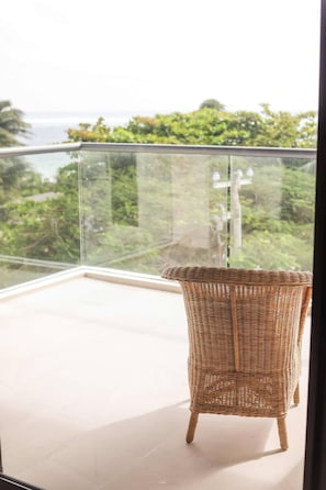 A wicker chair on a balcony with a glass railing, overlooking a green landscape. - PH Tucán: Private Terrace and Ocean View rooftop (Puerto Morelos)