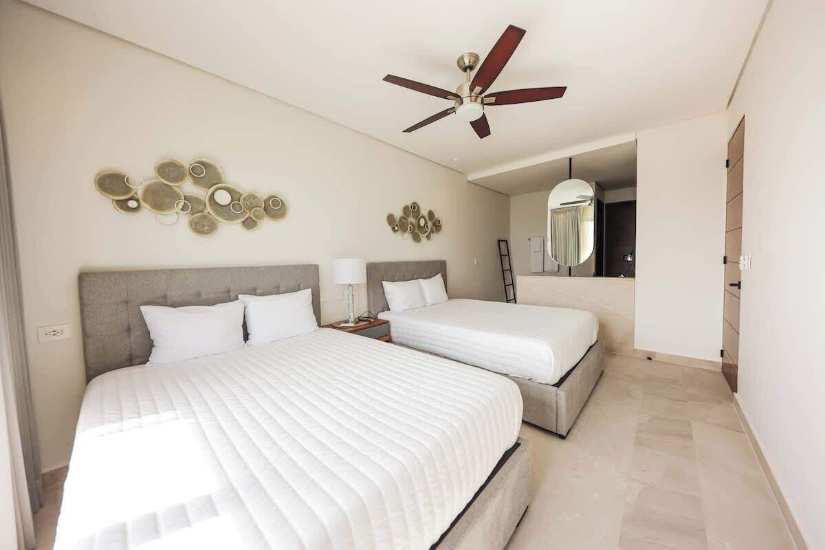 A hotel room with two beds, a ceiling fan, wall decor, and a mirror.