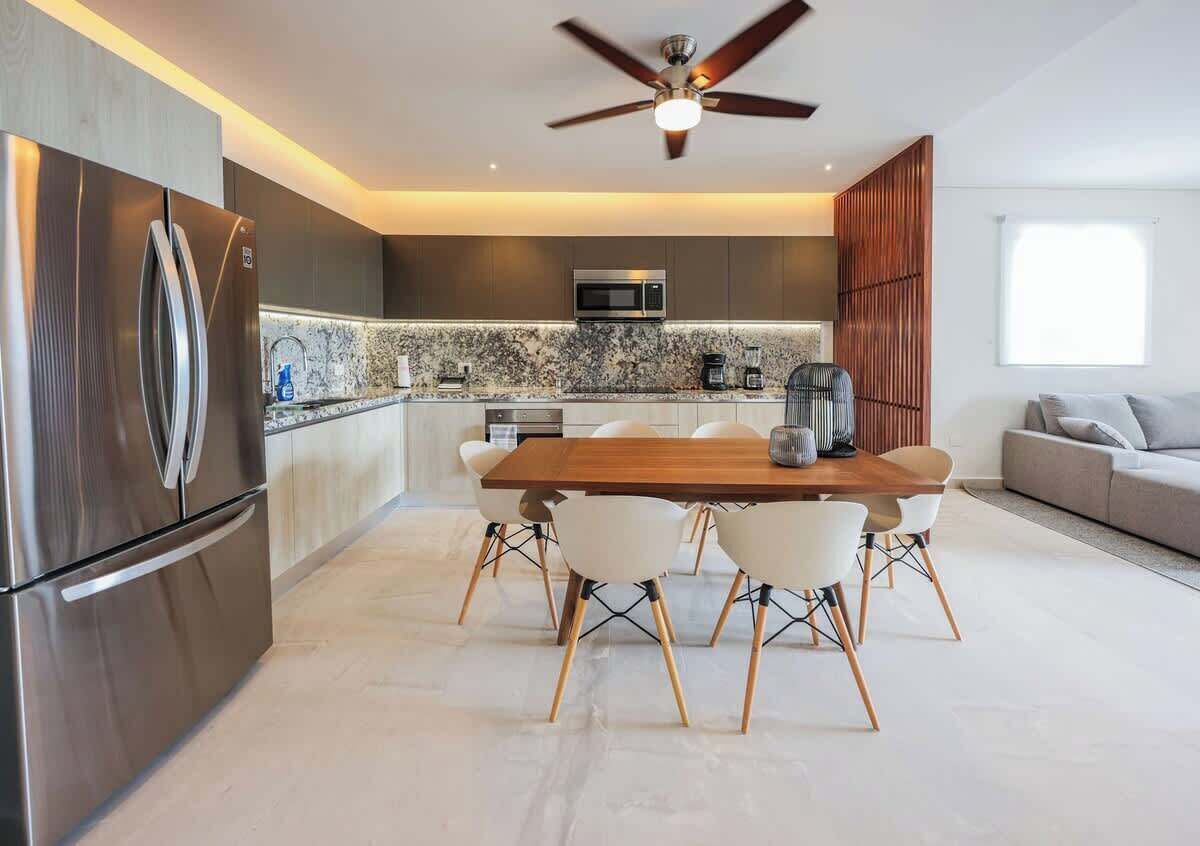 A modern kitchen with a built-in microwave, stainless steel refrigerator, and a dining area with a wooden table and white chairs.