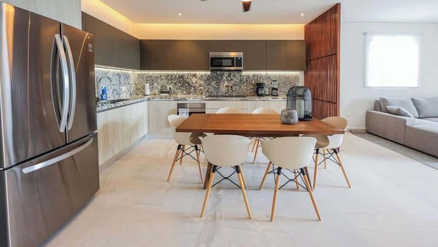 A modern kitchen with a built-in microwave, stainless steel refrigerator, and a dining area with a wooden table and white chairs. - PH Tucán: Private Terrace and Ocean View rooftop (Puerto Morelos)