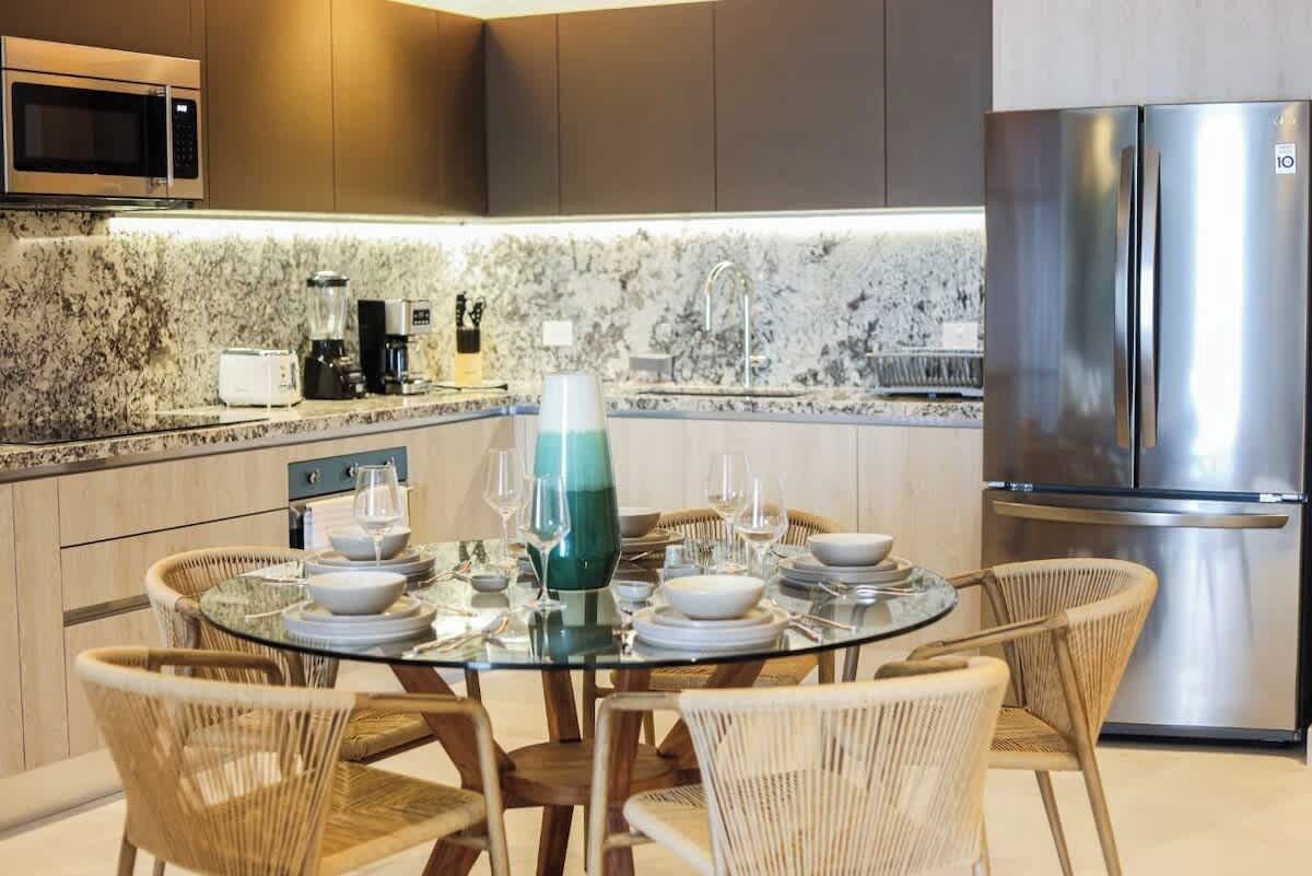 Eine moderne Küche mit einem runden Glastisch, gedeckt für das Essen, ausgestattet mit einem Mixer, Toaster und Edelstahlgeräten.