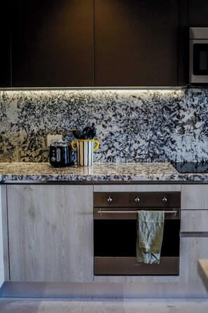 A kitchen with a granite countertop, a toaster, a mug, and a towel hanging over the oven. - Apt Quetzal: Coastal retreat, Shared Rooftop & Poo (Puerto Morelos)