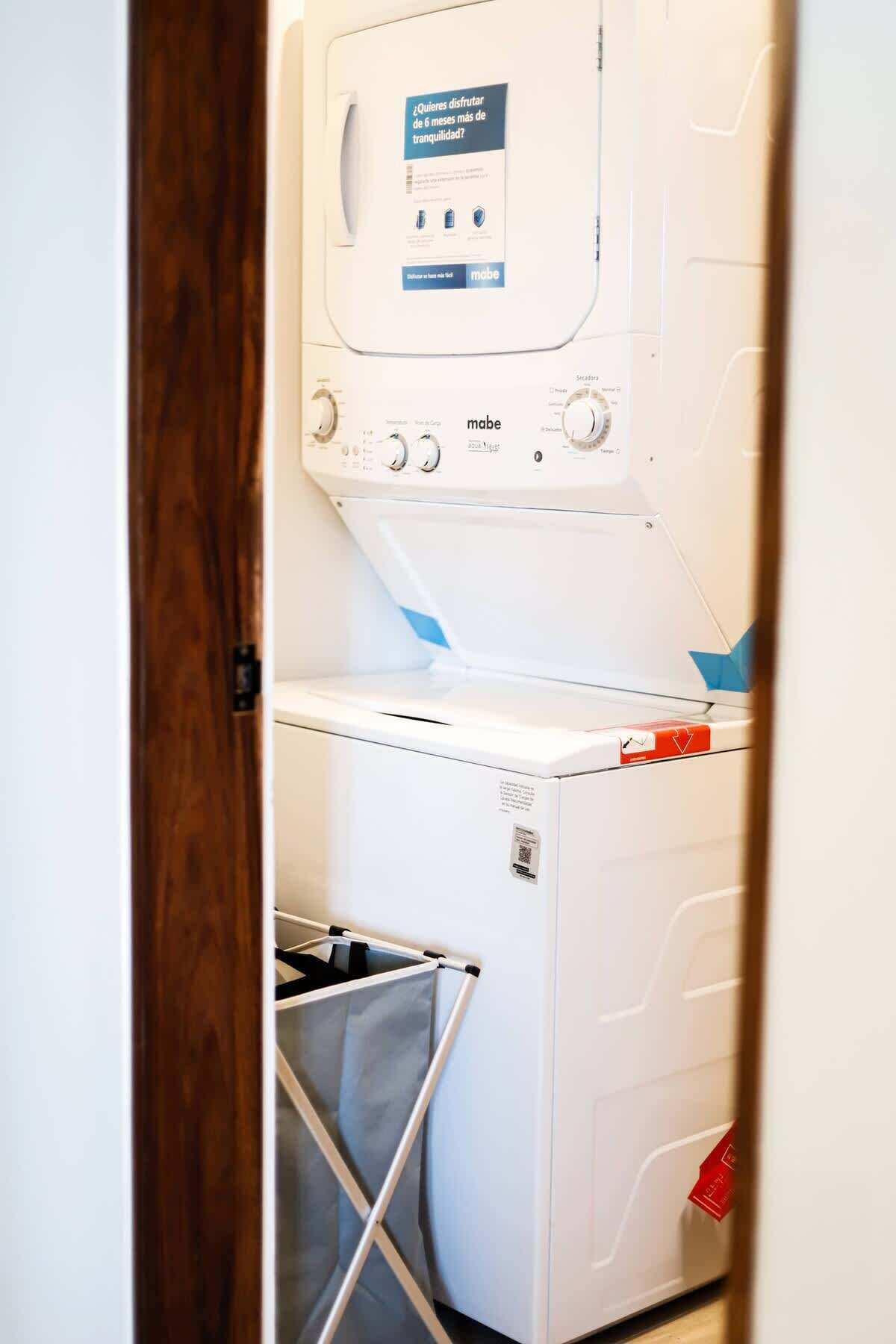 Een wasserette met een wasmachine, een droger en een metalen wasmand.