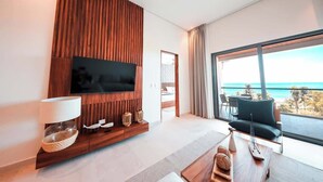 A modern living room with a flat-screen TV, wooden paneling, a large window with a view of the ocean, and a seating area with a table. - Apt Jaguar: Balcony with Sea View & Rooftop Pool (Puerto Morelos)