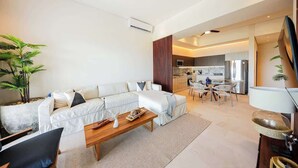 A modern living room with a sofa, coffee table, and a dining area with chairs. - Apt Jaguar: Balcony with Sea View & Rooftop Pool (Puerto Morelos)