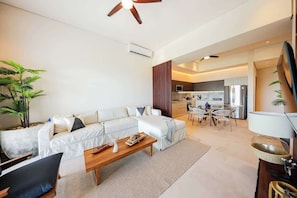 A modern living room with a sofa, coffee table, and a dining area with chairs. - Apt Jaguar: Balcony with Sea View & Rooftop Pool (Puerto Morelos)