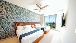 A hotel room with two beds, a ceiling fan, a large window with a view, and a TV mounted on the wall. - Apt Jaguar: Balcony with Sea View & Rooftop Pool (Puerto Morelos)