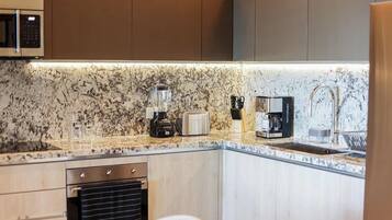 A modern kitchen with a granite countertop, a built-in oven, a coffee maker, and a microwave.