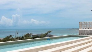 Una piscina infinita en la azotea con vista al océano y un muelle distante.