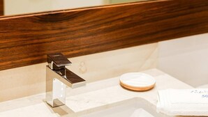 Un baño con lavabo blanco, espejo con marco de madera y un perchero para toallas.