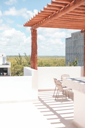 An outdoor patio with a pergola, a dining area with chairs, and a view of a distant landscape. - Apt Mantarraya: Private Plunge Pool & Terrace (Puerto Morelos)