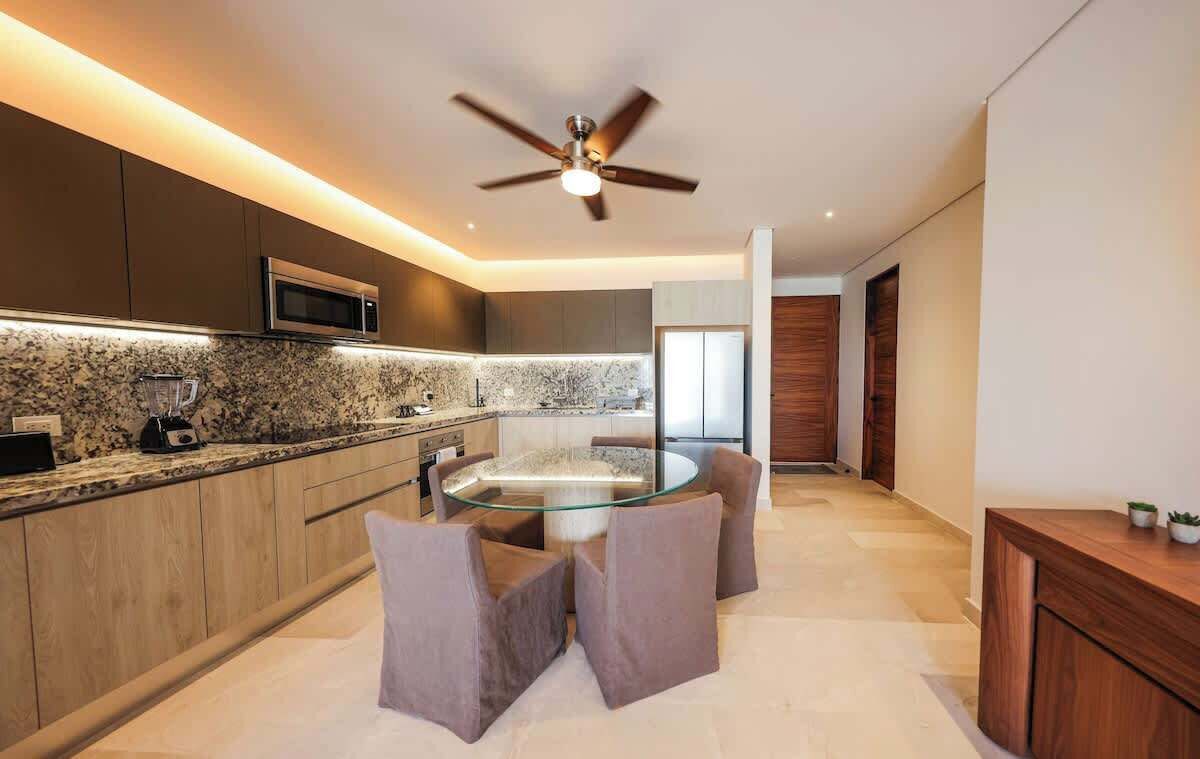 Una cocina moderna con una mesa de vidrio, armarios de madera y un ventilador de techo.