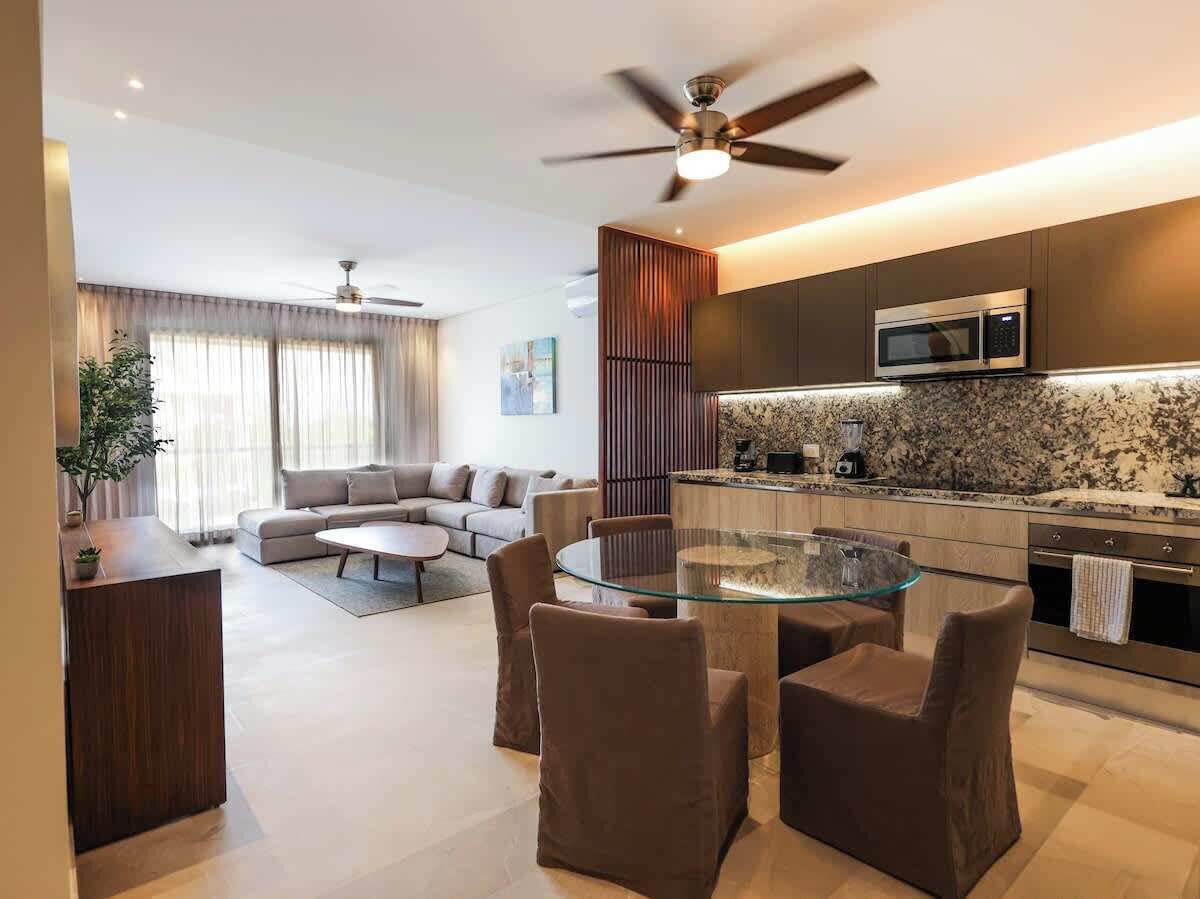 A modern living room with a glass dining table, a sofa, and a kitchen area with a microwave.
