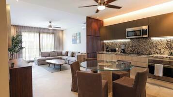 A modern living room with a glass dining table, a sofa, and a kitchen area with a microwave.