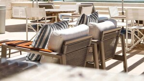 Eine Strandlounge mit Sitzgelegenheiten im Freien, zwei Sonnenschirmen und Blick auf das Meer.