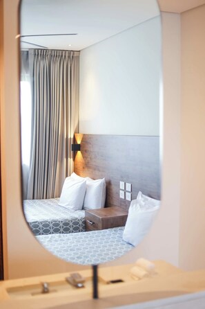 Hotellihuone, jossa on sänky, yöpöytä ja peili, joka heijastaa huonetta.