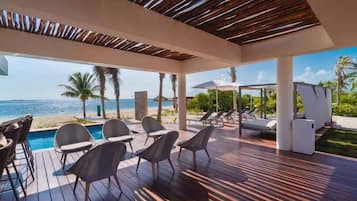 A covered outdoor area with a pool, lounge chairs, and a view of the beach.