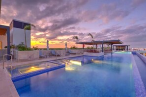 A swimming pool with lounge chairs and a covered seating area, surrounded by a modern building. - La Amada | Condo w Gorgeous Pool & Marina Views (Cancún)