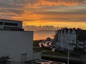 Rannikon auringonlasku, jossa näkyy rakennuksia ja tie.
