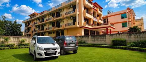 A multi-story residential building with a flat roof, balconies, and a parking area with two cars.