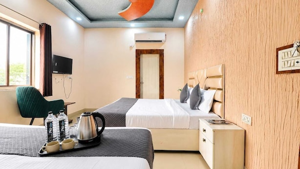 Quarto de hotel com duas camas, uma mesa de trabalho, uma cadeira, cafeteira e um relógio na parede.