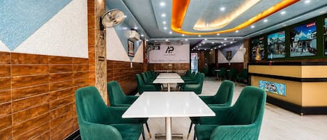 A restaurant interior with green upholstered chairs, white tables, and a modern ceiling design.
