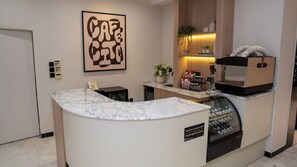 Ein moderner Empfangsbereich mit Marmorzauber, einer Kaffeemaschine und einem Schild, das anzeigt, dass das Café rund um die Uhr geöffnet ist.