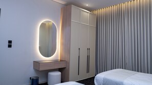 A hotel room with a bed, a bedside table, a mirror, a wardrobe, and a curtain. - Darina Serviced Apartments2 (Riyadh)