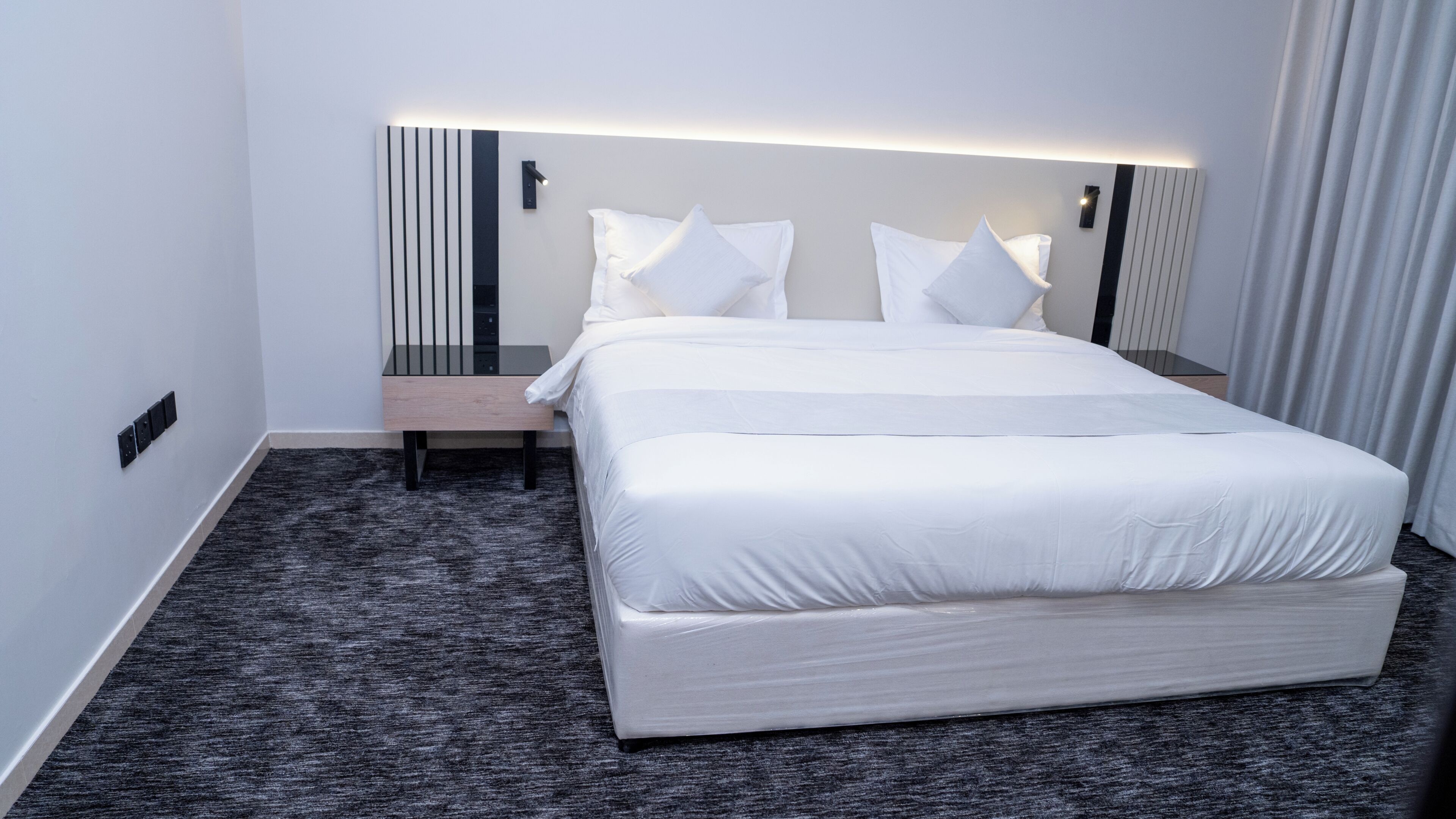 A hotel room with a large bed, bedside tables, a nightstand, and a wall-mounted light fixture.