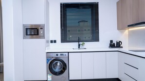 A modern kitchen with a built-in washing machine, a microwave, and a sink. - Darina Serviced Apartments2 (Riyadh)