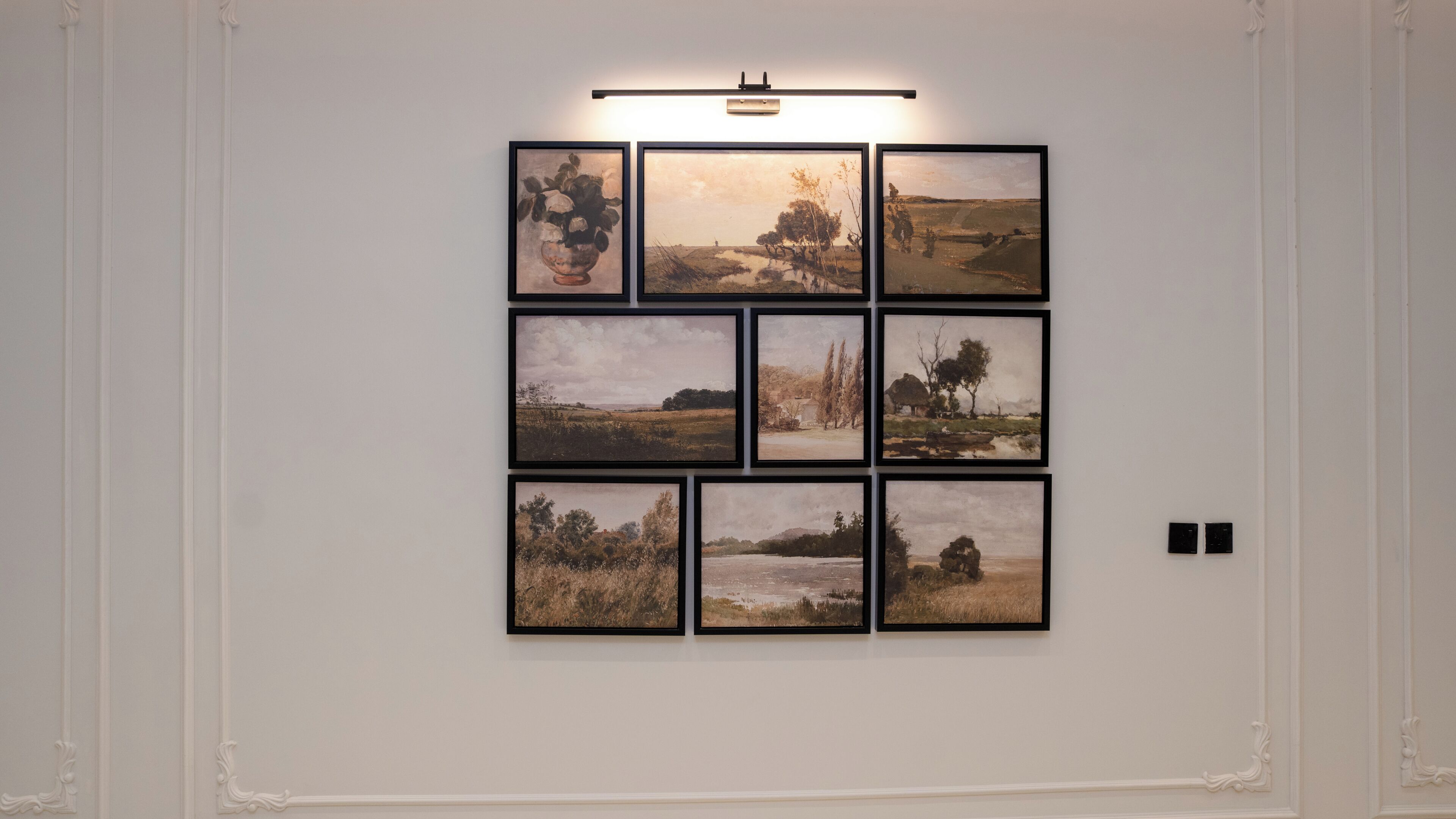 A wall with nine framed landscape paintings arranged in a 3x3 grid.