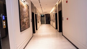 Ein Hotelkorridor mit Marmorboden, gerahmten Kunstwerken an den Wänden und einem digitalen Bedienfeld für den Aufzug.