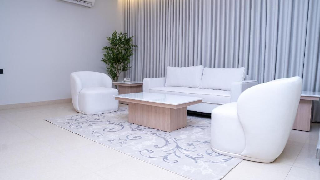 A modern living room with a white sofa, two white armchairs, and a wooden coffee table.