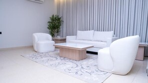 A modern living room with a white sofa, two white armchairs, and a wooden coffee table. - Darina Serviced Apartments (Riyadh)
