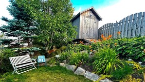 Un jardin avec un abri en bois, un banc et diverses plantes.