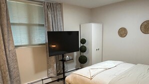 Une chambre à coucher comprenant un lit, une télévision, une armoire et une fenêtre avec des rideaux.