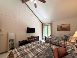 Ein Schlafzimmer mit zwei Betten, einem Fernseher, einem Fenster mit Vorhängen und einem Bild an der Wand.