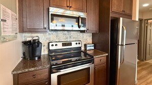 Una cocina con gabinetes de madera oscura, un microondas de acero inoxidable, una estufa negra y un refrigerador plateado.