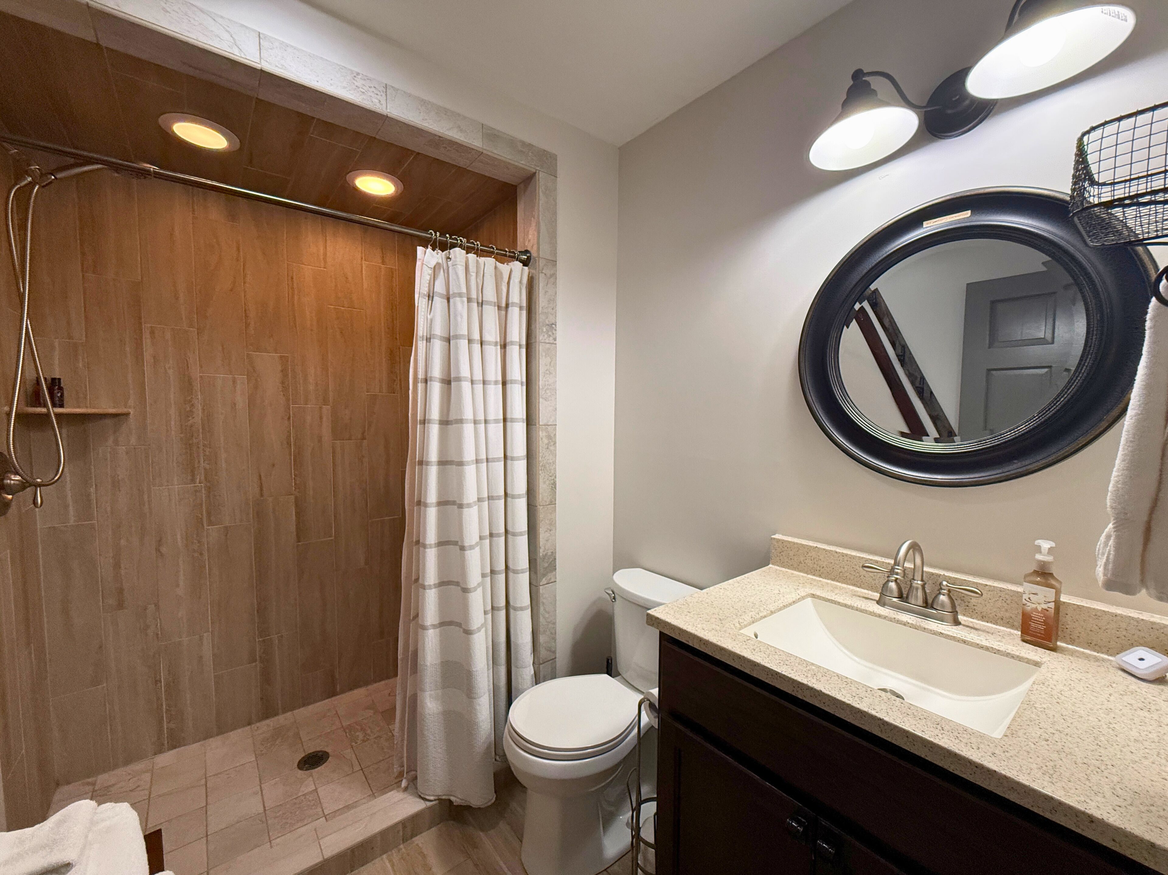A bathroom with a shower, toilet, sink, and a mirror.