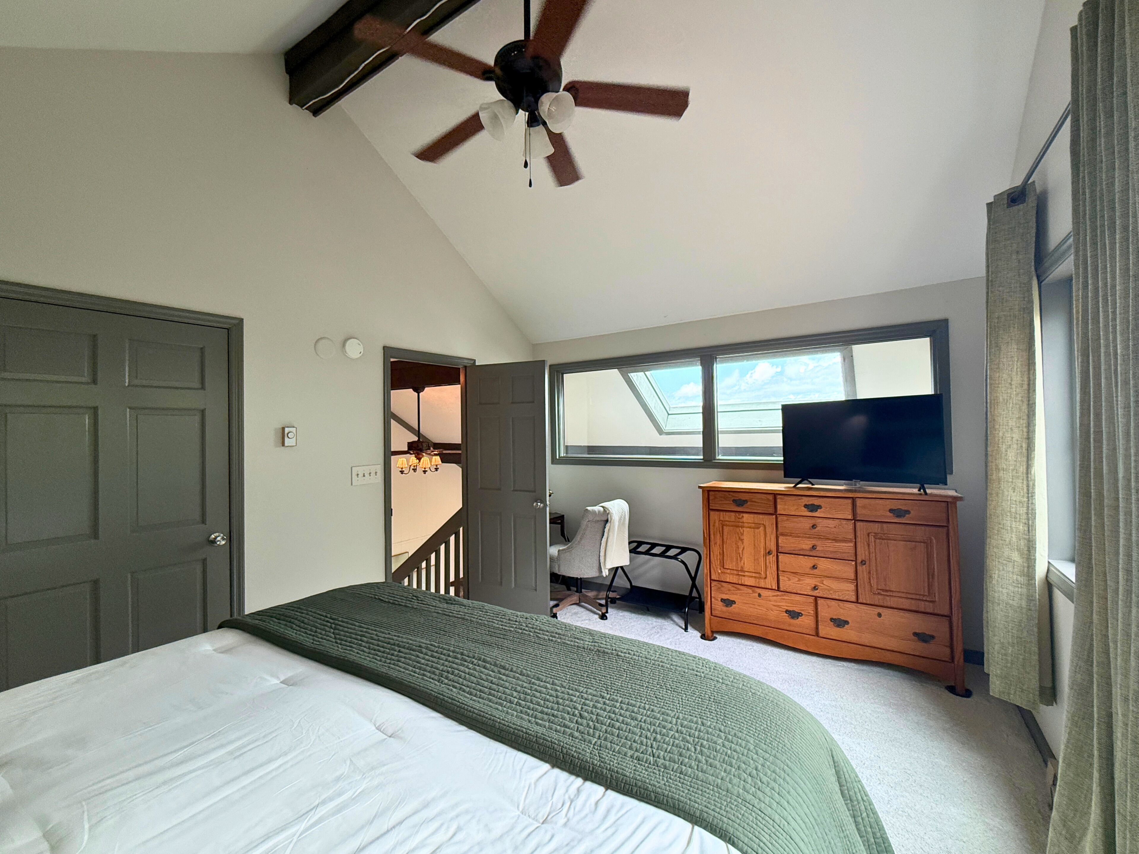 A bedroom with a bed, a ceiling fan, a dresser, a television, and a window.
