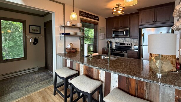 Una cocina con una isla central, taburetes de bar, microondas, estufa y refrigerador.