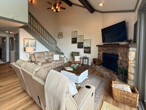 A spacious living room with a fireplace, a large television, and a staircase leading to another level. - breathtaking long-range views and contemporary décor,  3-bed, 2-bath condo (Sugar Mountain)
