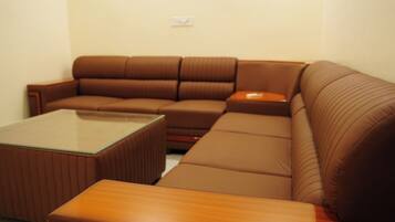 A brown leather sofa with a glass coffee table and a wooden side table in a room with plain walls.